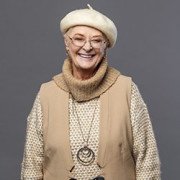 Woman with glasses dressed in beige outfit including beret and smiling at camera